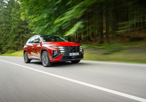 červený Hyundai TUCSON jedoucí podél lesa