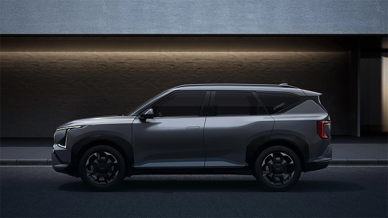 Šedý model nové Kia EV5 - boční pohled na osvětlený vůz za šera, zaparkovaný před budovou