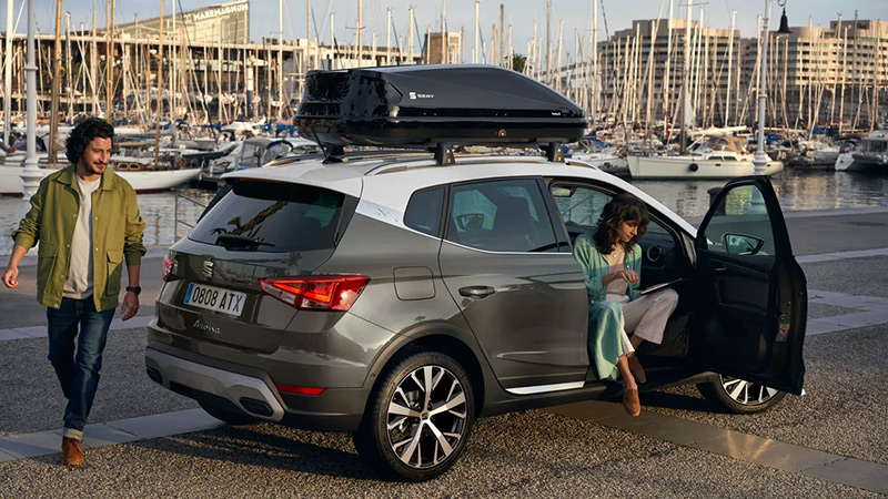 SEAT Arona zaparkovaný v přístavu, muž ho obchází a žena sedí jako spolujezdec s otevřenými dveřmi