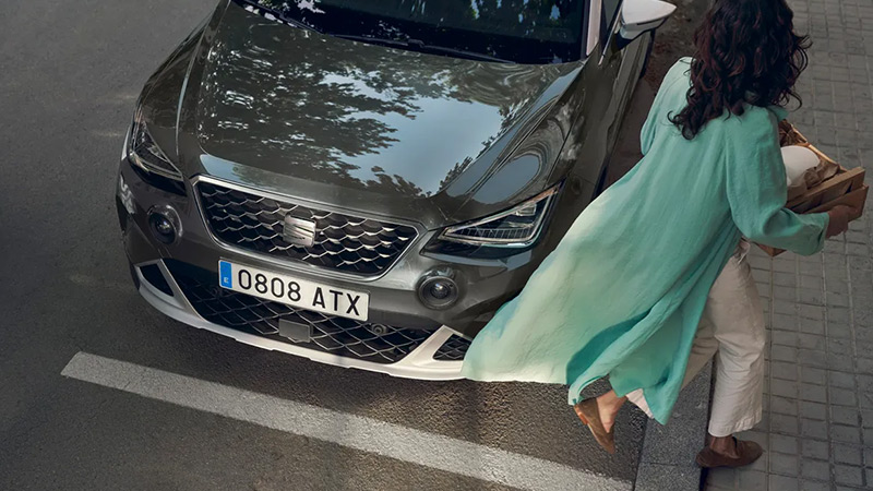 Žena prochází kolem zaparkovaného vozu SEAT Arona