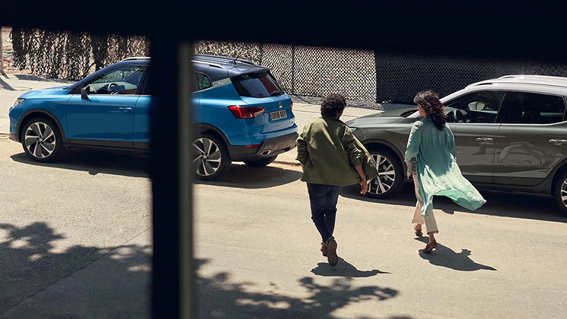 Dva vozy SEAT Arona zaparkované u chodníku, přichází k nim muž a žena