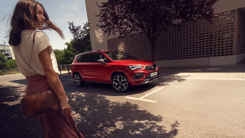 K zaparkovanému červenému vozu SEAT Ateca přichází žena