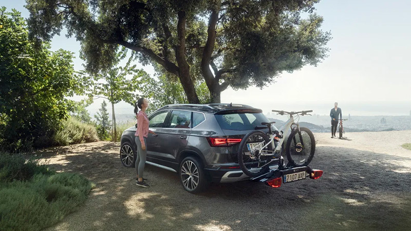 Zaparkovaný šedý SEAT Ateca s nosičem kol a připevněným kolem